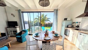 Un salon moderne avec une table à manger en bois, des chaises blanches, un canapé bleu et un téléviseur.