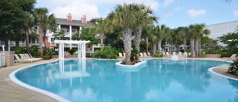 A swimming pool with lounge chairs and palm trees, surrounded by a brick building with a white porch.