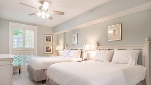 Une chambre avec deux lits, un ventilateur de plafond et des œuvres d’art accrochées aux murs.