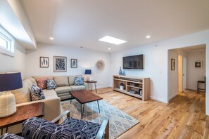 A modern living room with a sofa, coffee table, and TV stand. - East Virginia Blues Condo, Walk to Beach & Shops (Cape Charles)