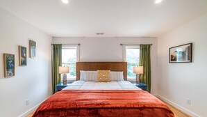 A bedroom with a large bed, two bedside tables, green curtains, and artwork on the walls.