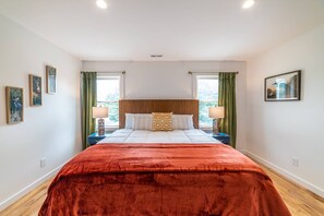 Une chambre à coucher avec un grand lit, deux tables de chevet, des rideaux verts et des œuvres d’art accrochées aux murs.
