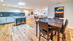 A modern kitchen with a dining area, featuring a wooden floor, blue bar stools, and a dining table with placemats. - East Virginia Blues Condo, Walk to Beach & Shops (Cape Charles)