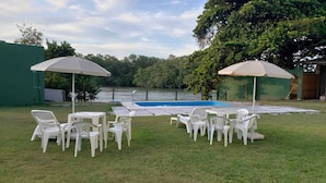 Zona piscina con sedie e tavoli di plastica bianca, una piscina e vista su un lago.