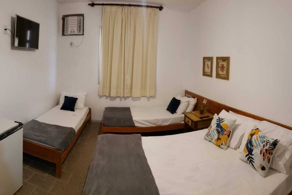 Habitación de hotel con dos camas individuales, un refrigerador pequeño, un televisor y una ventana con cortinas.