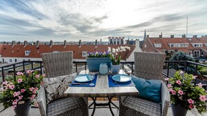 Una terraza en la azotea con mobiliario de mimbre, una mesa preparada para dos personas y plantas en macetas.