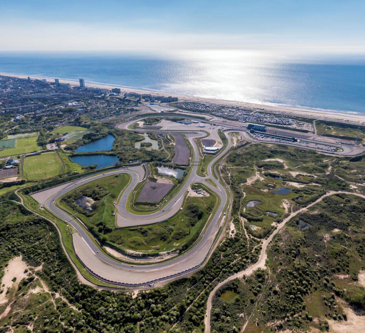 Vista aérea de uma área costeira com uma estrada sinuosa, uma praia e uma grande extensão de água.