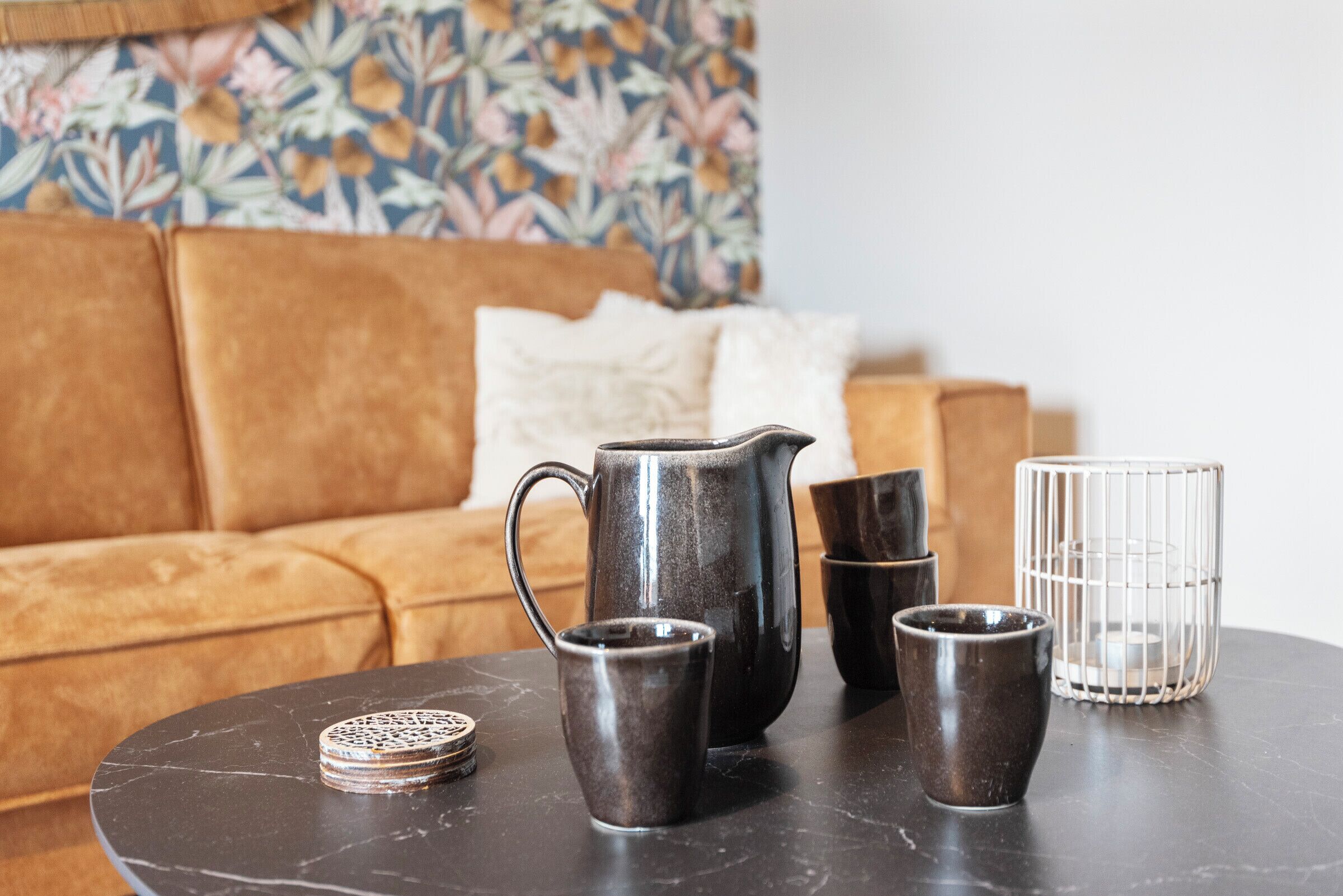 Een ronde tafel met een donker marmeren blad, een metalen karaf, twee kleine bekertjes en een glazen pot.