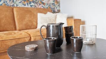 Een ronde tafel met een donker marmeren blad, een metalen karaf, twee kleine bekertjes en een glazen pot.