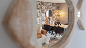 Un coin repas avec une table en bois, des chaises, un miroir rond et un papier peint à motifs floraux.