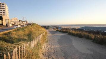 A coastal walkway with a wooden fence, a paved path, and buildings in the background.