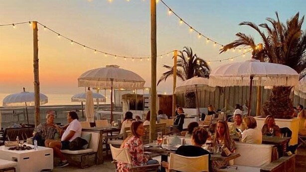 Un espace extérieur aménagé pour les repas, avec des tables, des chaises, des parasols et des guirlandes lumineuses.