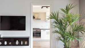 Une cuisine moderne avec des meubles blancs, un four encastré et un téléviseur à écran plat fixé au-dessus d’une console sombre agrémentée d’objets décoratifs.