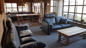 Un soggiorno accogliente con un divano, una poltrona in pelle e un tavolino in legno. Si nota, sullo sfondo, una zona pranzo con tavolo e sedie.