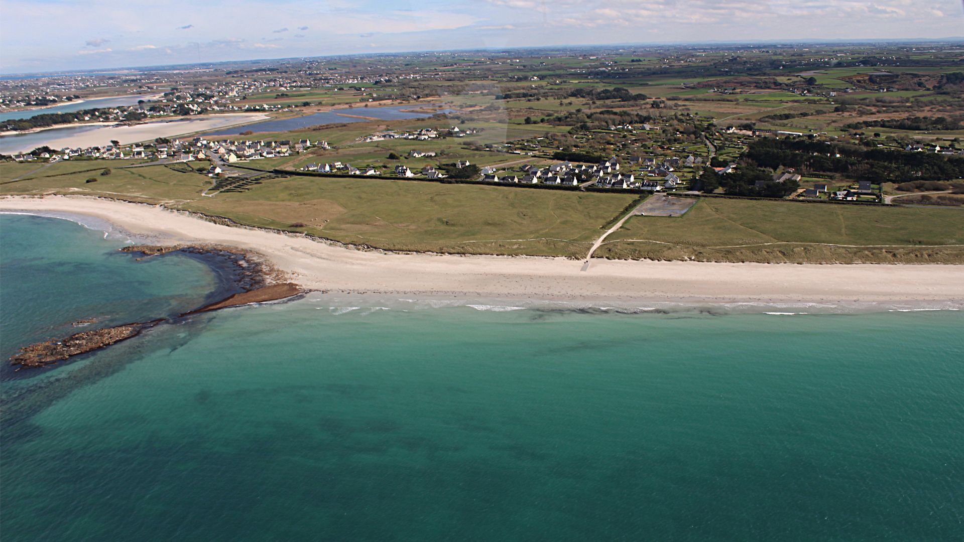Vista aérea de una zona costera con playa, un río y casas dispersas.