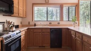 A kitchen with wooden cabinets, a black stove, a dishwasher, and a window with a view of trees. - Lakeshore Villa (Incline Village)