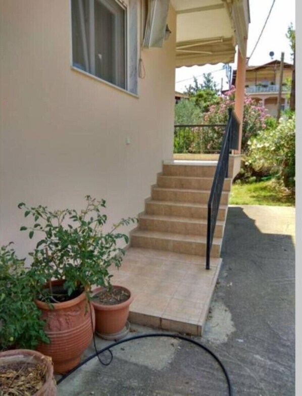 Une maison dotée d’un porche abrité, d’un escalier menant à un balcon et de plantes en pot.