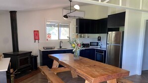 A modern kitchen with a wooden table, black cabinets, and stainless steel appliances. - Strath Creek Lodge at The Village Green (Strath Creek)