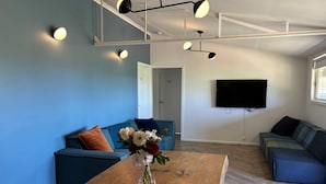 A modern living room with a wooden coffee table, blue sofas, and a flat-screen TV mounted on the wall. - Strath Creek Lodge at The Village Green (Strath Creek)