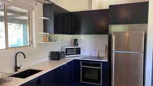 A modern kitchen with dark blue cabinets, a stainless steel refrigerator, a microwave, and an oven. - Strath Creek Lodge at The Village Green (Strath Creek)