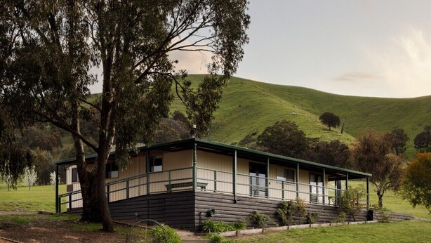 A two-story house with a porch, surrounded by a grassy landscape and trees. - Strath Creek Lodge at The Village Green (Strath Creek)