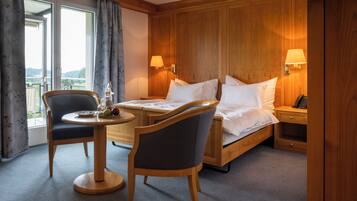 A hotel room with a bed, two chairs, a small table with fruit, a lamp, and a view of the outdoors.