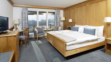 Ein Hotelzimmer mit einem großen Bett, einem Holzkopfende, einem Schreibtisch mit Stuhl, einem kleinen Tisch und einem Fernseher.