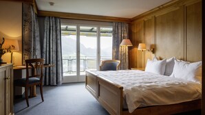 Une chambre d’hôtel avec un lit en bois, un bureau avec une chaise, un balcon avec des rideaux et une vue sur les montagnes.