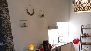 A compact kitchen with a microwave, toaster, and coffee maker. A red chair and a round wooden table are in the foreground. The kitchen has a tiled backsplash and a hanging light fixture. - L'Étoile - studio in the heart of Chinon (Chinon)