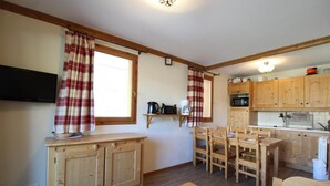 A compact kitchen with wooden cabinets, a dining table, and a television. - 150m from shops, Ground floor, view mountain, fitness, swimming pool, balcony, tv, ski locker, 38m² (Lanslebourg-Mont-Cenis)