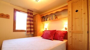 A bedroom with a bed, a window with curtains, a bookshelf, and a wooden wardrobe. - 150m from shops, Ground floor, view mountain, fitness, swimming pool, balcony, tv, ski locker, 38m² (Lanslebourg-Mont-Cenis)