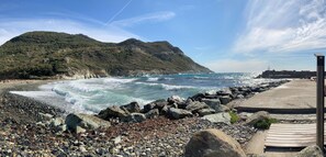 A rocky beach with waves crashing onto the shore, a wooden walkway, and a mountainous backdrop. - Village House (4–6 people) Cap Corse Barrettali, 5 min. from the beach (Barrettali)