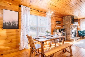Cozy cabin interior with a dining area, stone fireplace, and a framed picture on the wall.