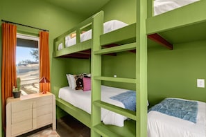 A bunk bed room with green walls, a window with orange curtains, and a bedside table with a lamp.