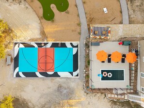 An aerial view of a property with a basketball court, outdoor seating area, and a pool.