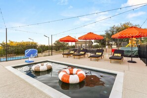 A swimming pool with lounge chairs and umbrellas, surrounded by a fence.