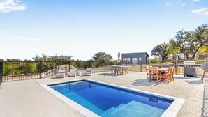 Une piscine avec des chaises longues et un espace barbecue, le tout entouré d’une clôture et d’arbres.