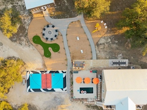 An aerial view of a property with a tennis court, a pool table, and a landscaped area with a unique green sculpture.