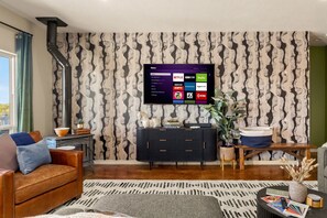A living room with a flat-screen TV mounted on the wall, a leather sofa, a coffee table, and a patterned rug.