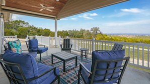 Une terrasse couverte, aménagée avec du mobilier d’extérieur et dotée d’un ventilateur de plafond, offrant une vue sur le paysage.