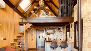 Een gezellige woonkamer met een bank, een salontafel en een open haard. Er is een keuken met een bar en krukken.