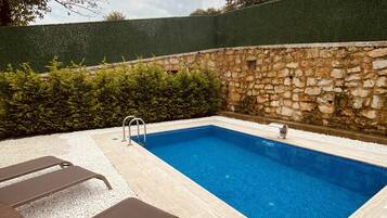 Una piscina rectangular con un muro de piedra y un seto verde al fondo.
