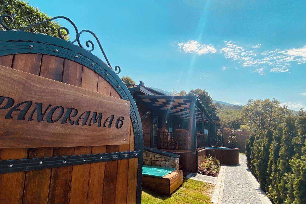 Un panneau en bois portant l’inscription « PANORAMA6 » et un sentier menant à un bâtiment dont le toit est à carreaux.