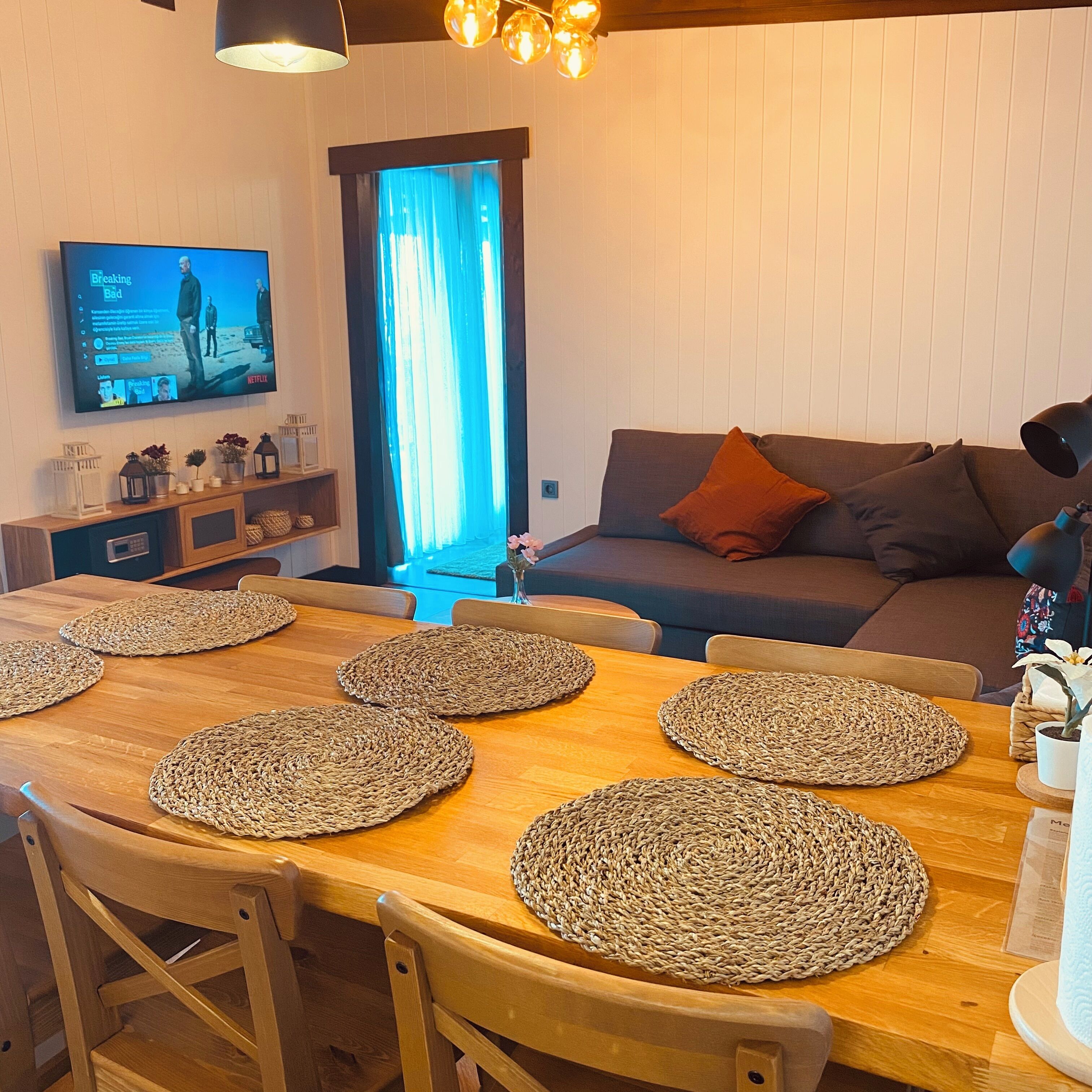 A cozy living room with a wooden dining table, a sofa, and a TV mounted on the wall.