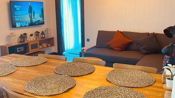 A cozy living room with a wooden dining table, a sofa, and a TV mounted on the wall.