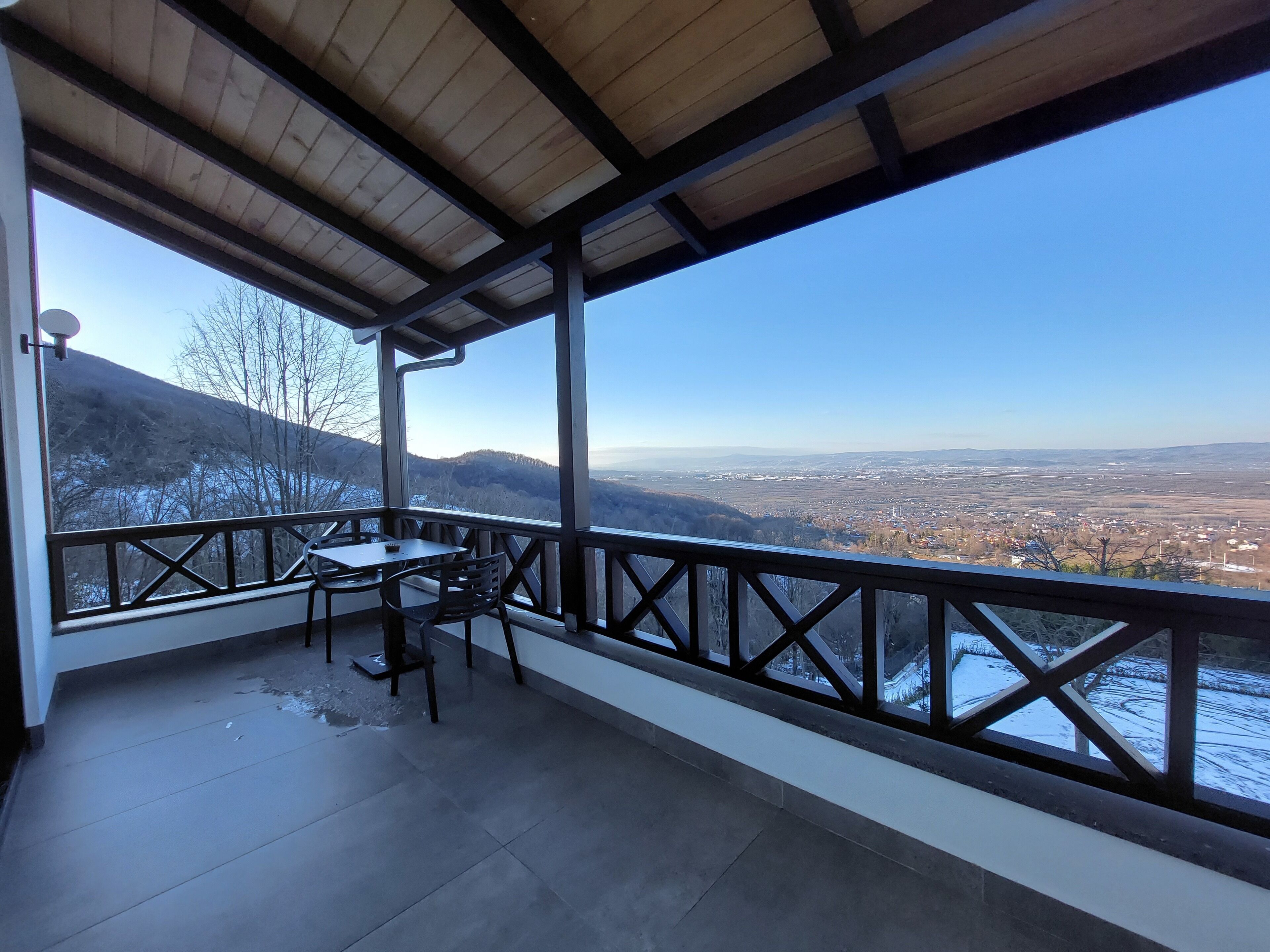 A covered outdoor area with a table and chairs, overlooking a valley and distant cityscape.