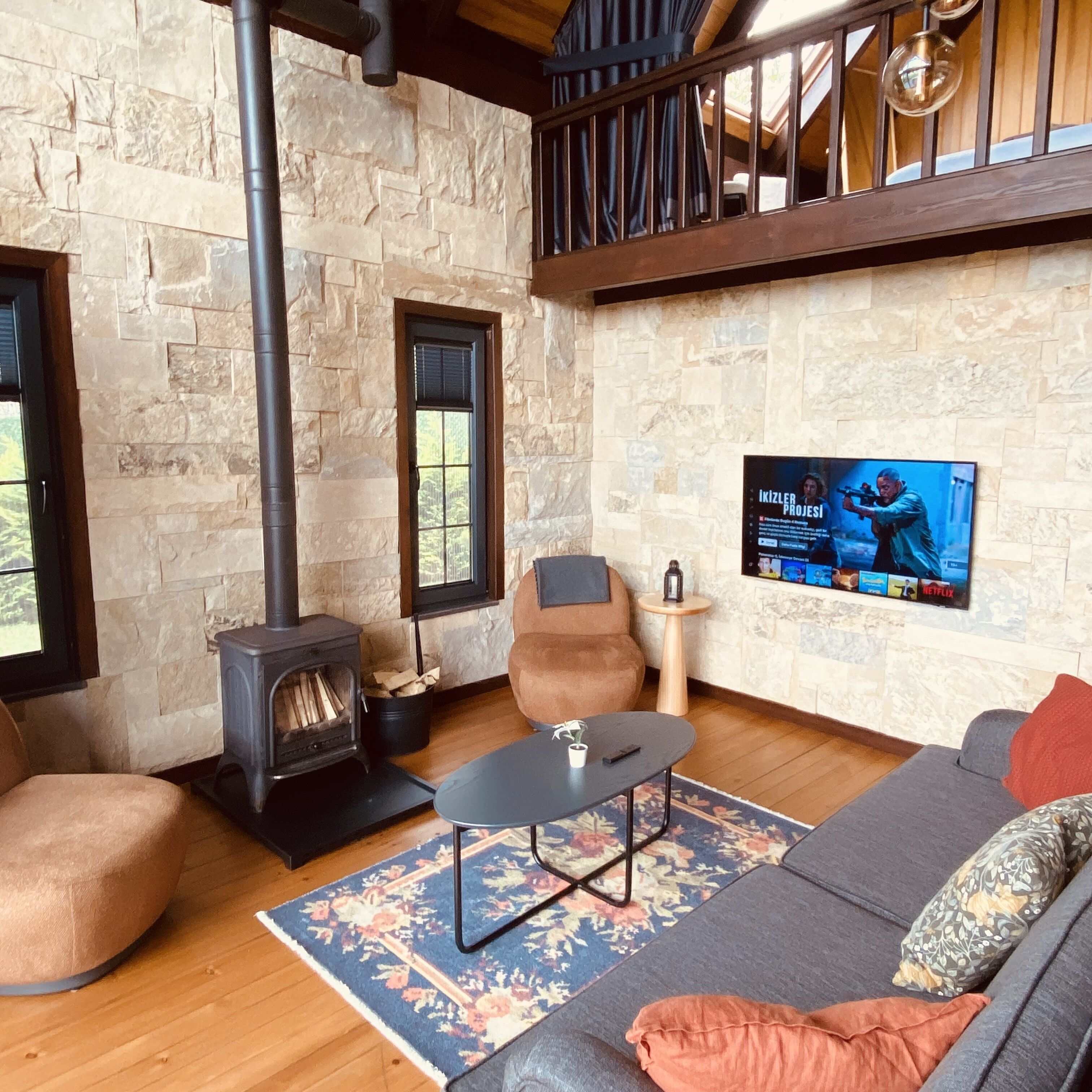 A cozy living room with a stone wall, a fireplace, a sofa, a coffee table, and a TV mounted on the wall.