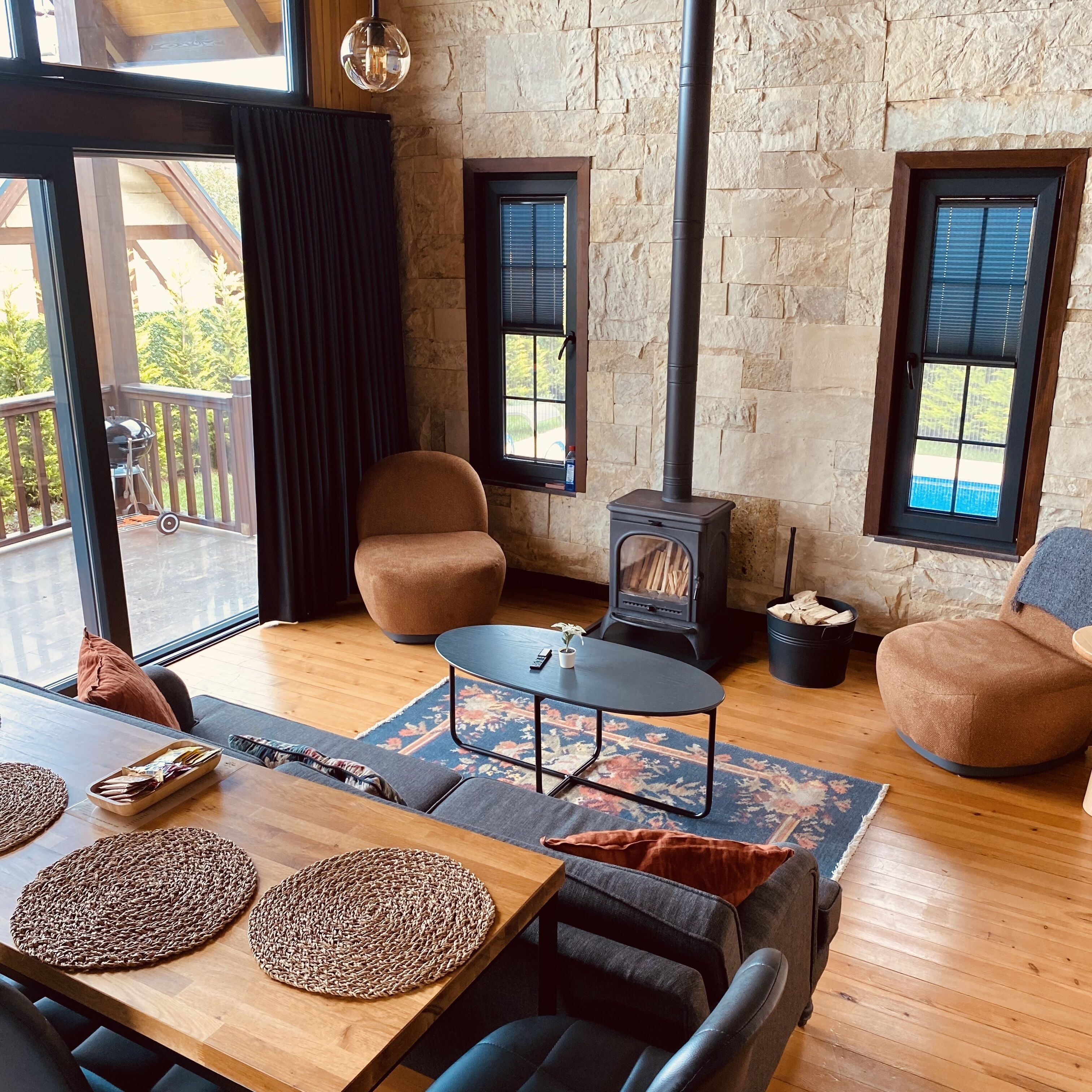 Ein gemütliches Wohnzimmer mit Steinwand, Kamin, bequemen Sitzmöglichkeiten und Blick ins Freie.