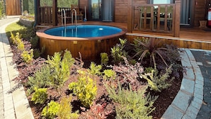 Een houten terras met een jacuzzi, omringd door een tuin met verschillende planten.