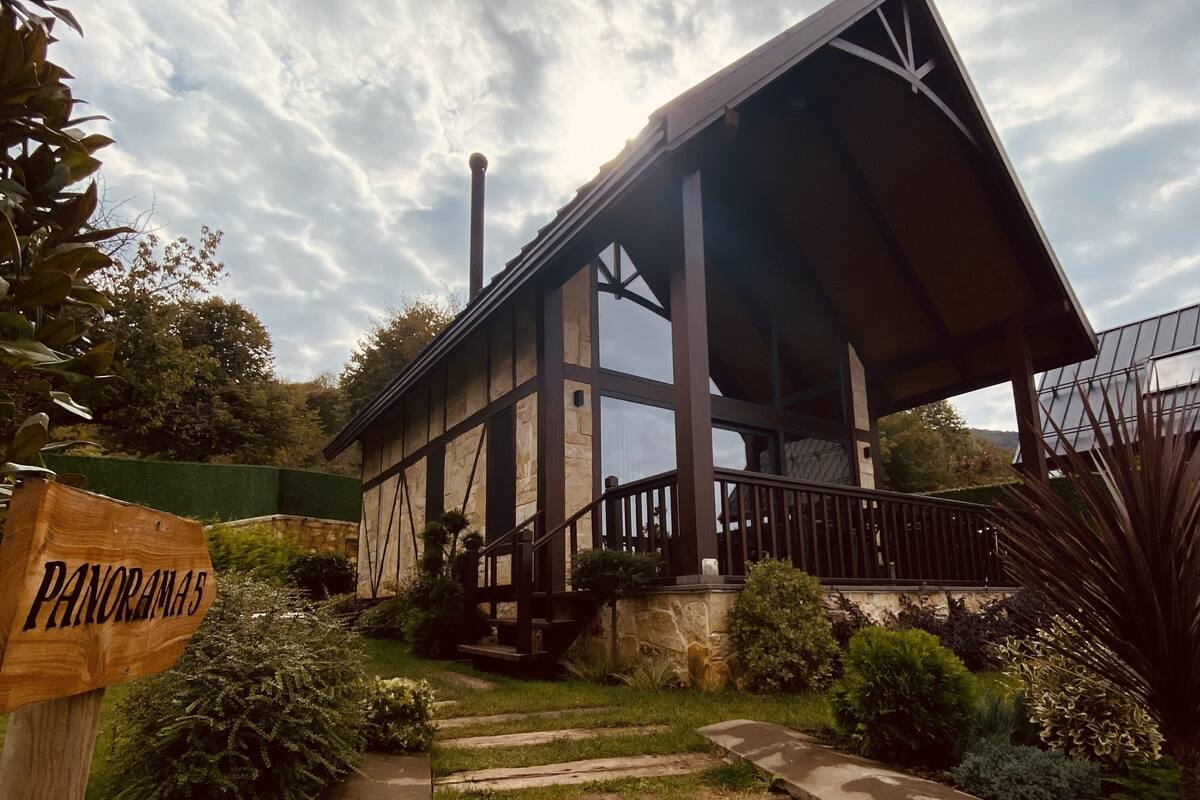 Une structure en bois, dotée d’un toit en pente et d’une base en pierre, entourée de verdure et accessible par un sentier.